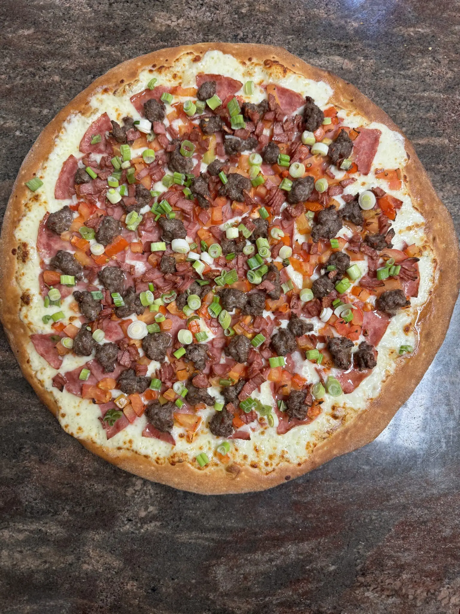 A fully topped pizza with sausage, green peppers, and tomatoes.