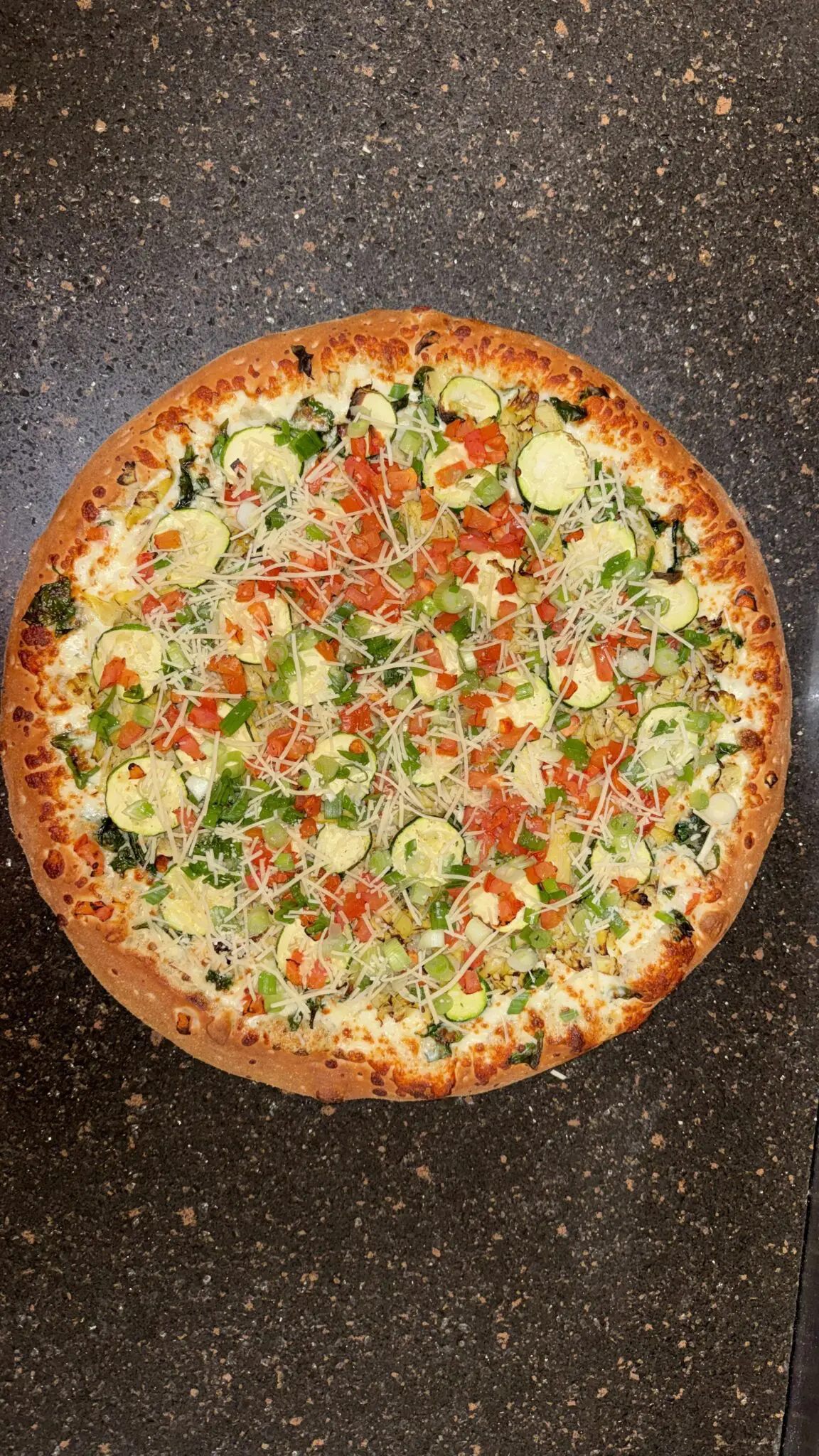 A veggie pizza topped with zucchini, tomatoes, and green herbs.