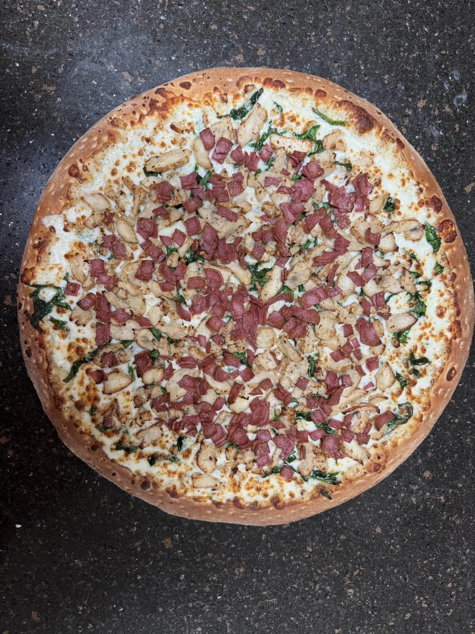 A large pizza topped with cheese, sausage, and spinach.