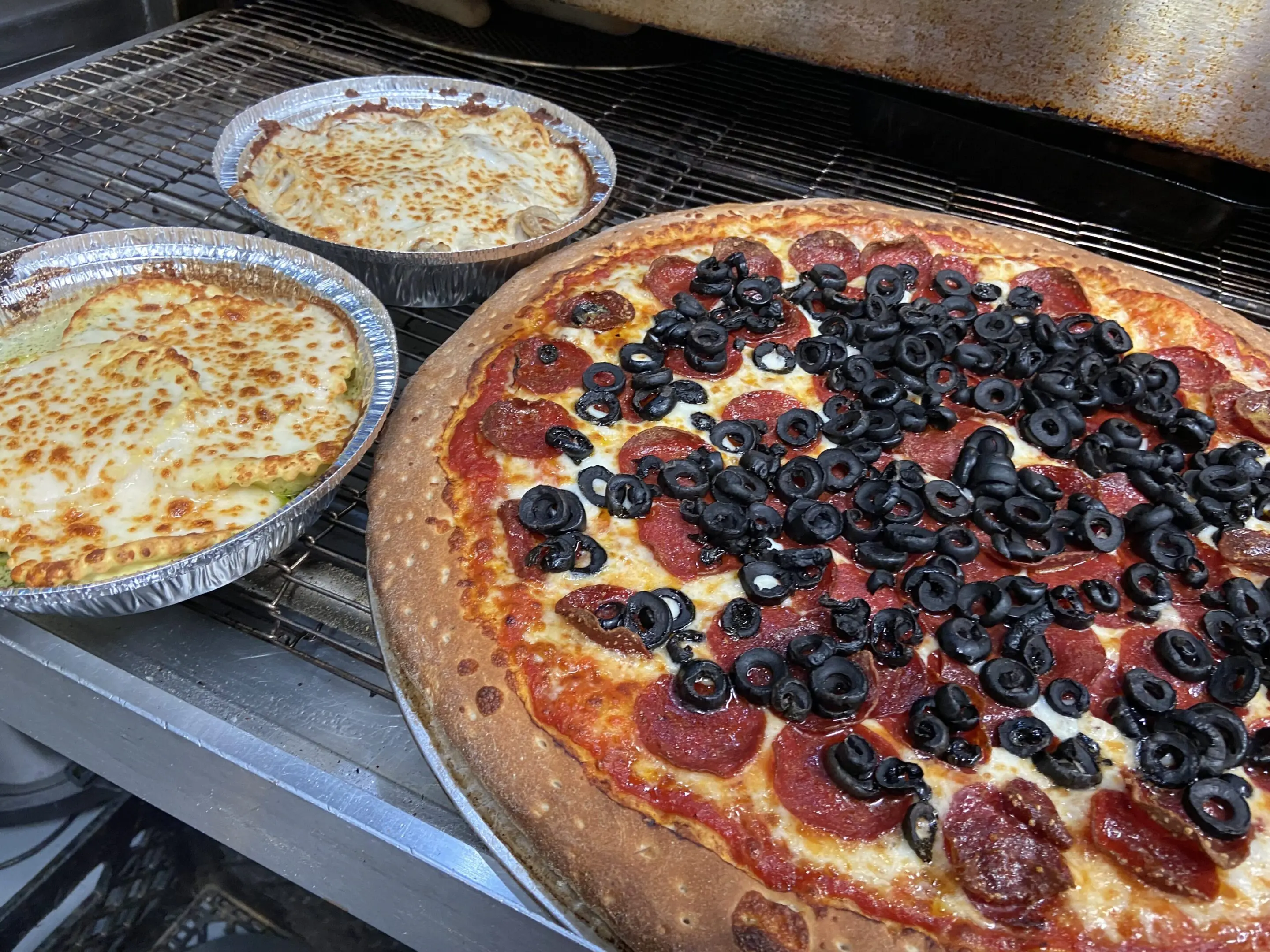 A large pizza topped with olives and pepperoni, alongside two baked pasta dishes.