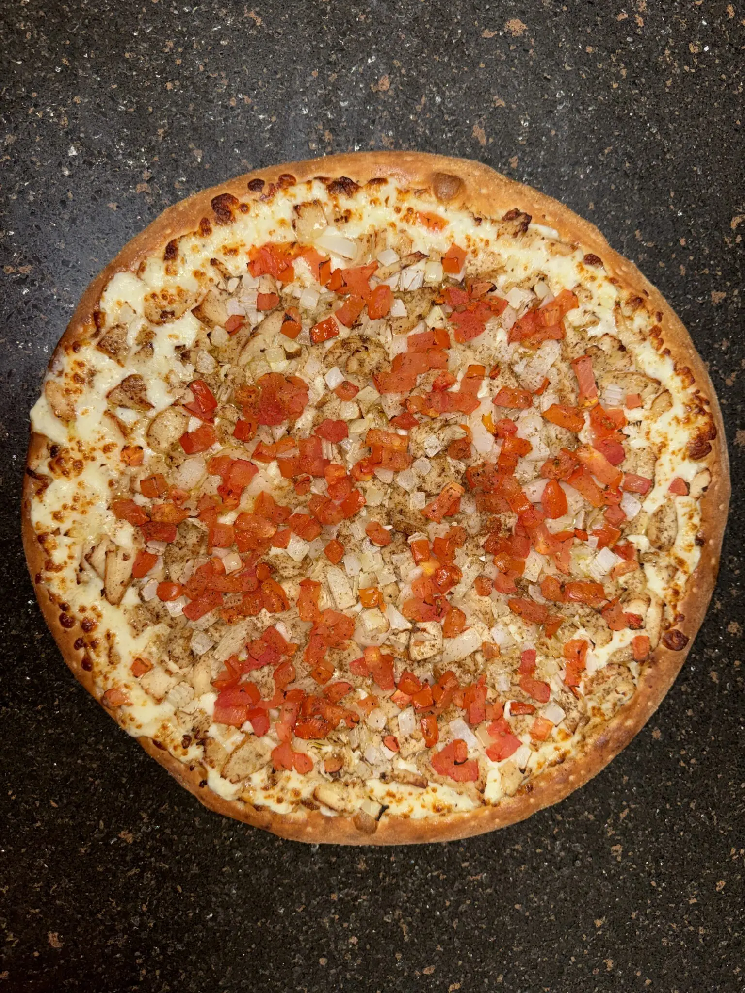 A whole pizza topped with diced tomatoes and cheese.