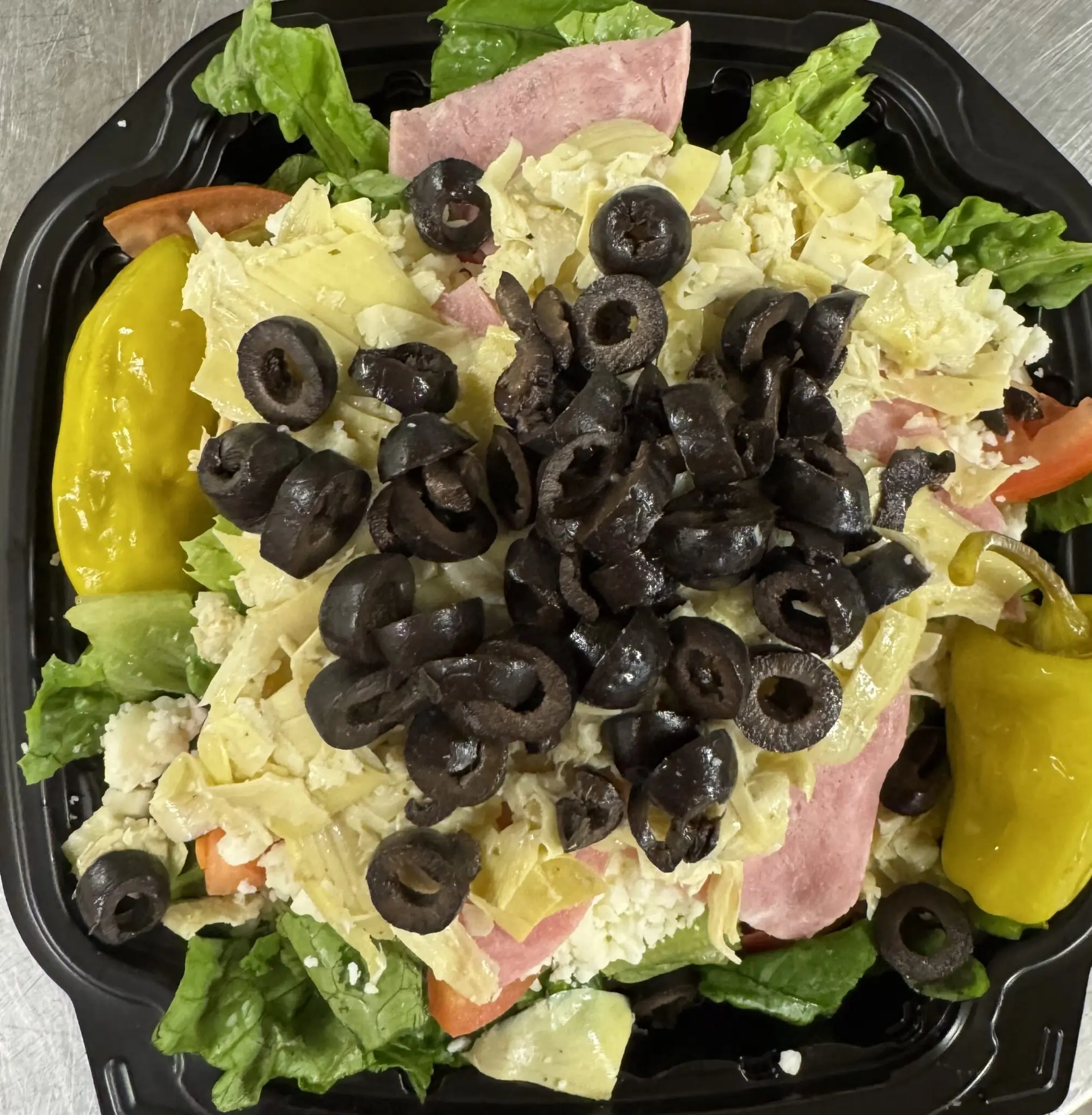 Fresh salad topped with black olives and ham.