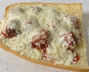 A meatball sandwich topped with melted cheese.