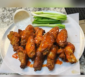 Plate of crispy buffalo chicken wings with dipping sauce and celery sticks.