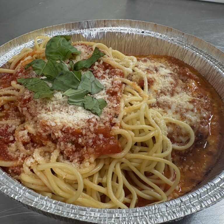 Spaghetti topped with tomato sauce, grated cheese, and fresh parsley in a foil container.
