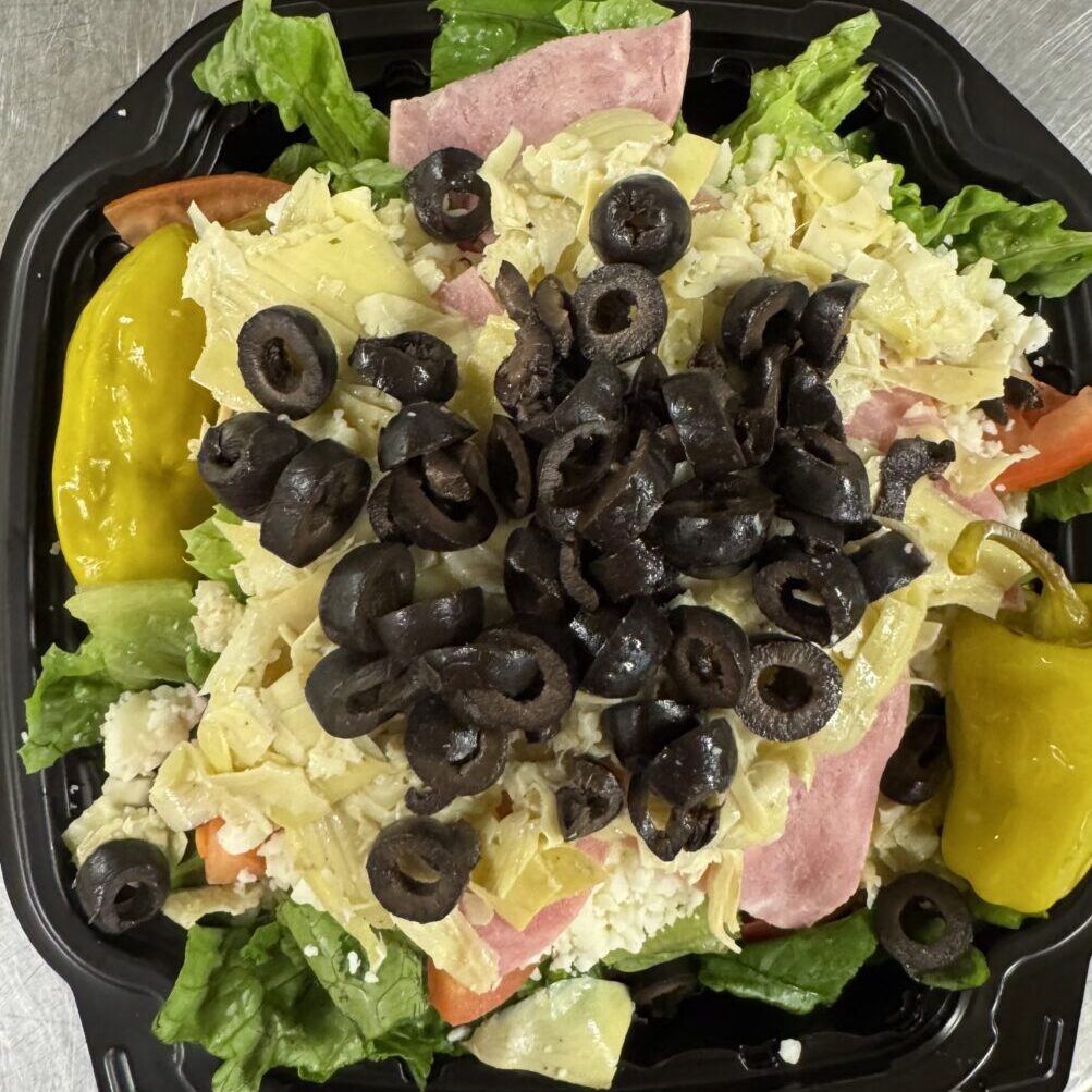 Fresh salad topped with black olives and ham.