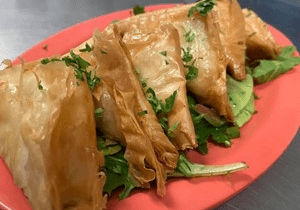 Golden fried samosas garnished with chopped herbs on a red plate.