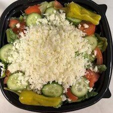 Fresh vegetable salad topped with crumbled cheese in a black bowl.