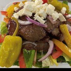 A colorful Greek salad with grilled meat and feta cheese.